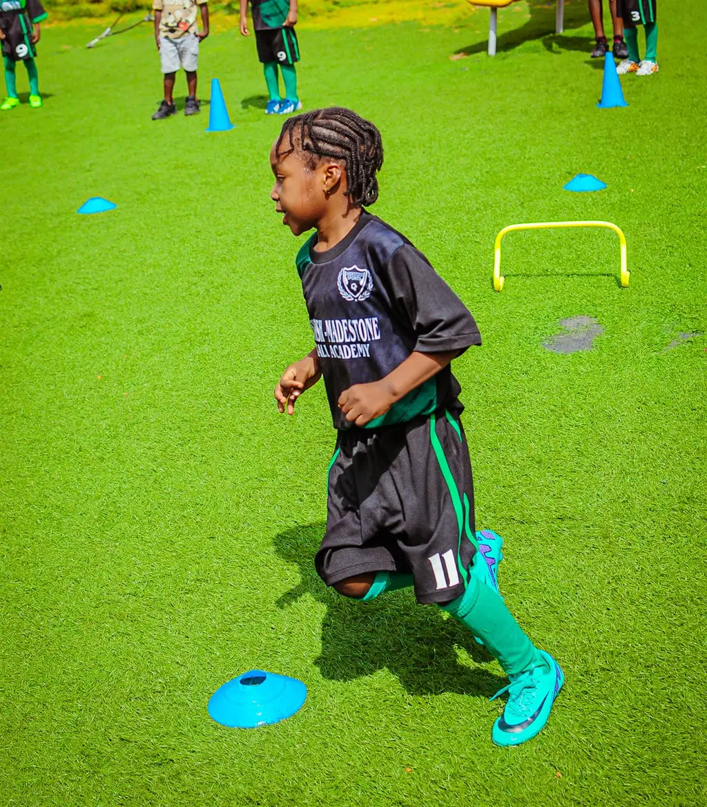 A young Madestone player in the academy kit sprinting through an agility cone drill on green turf